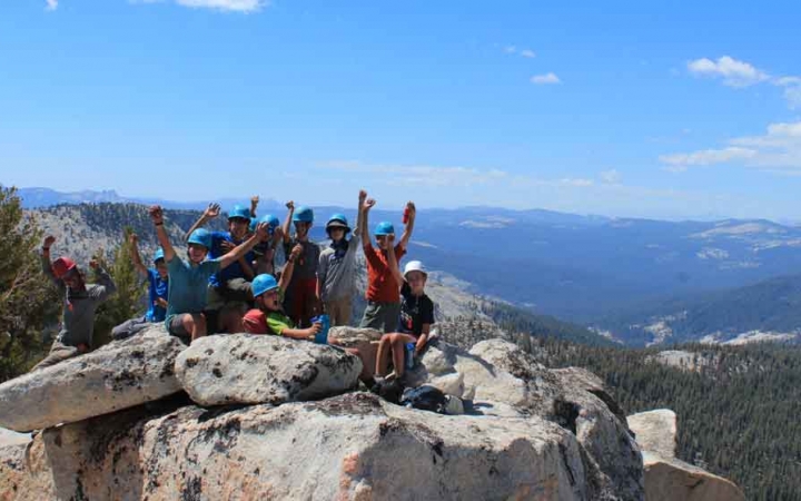 a group of students raise their hands in success at the top of a summit in yosemite